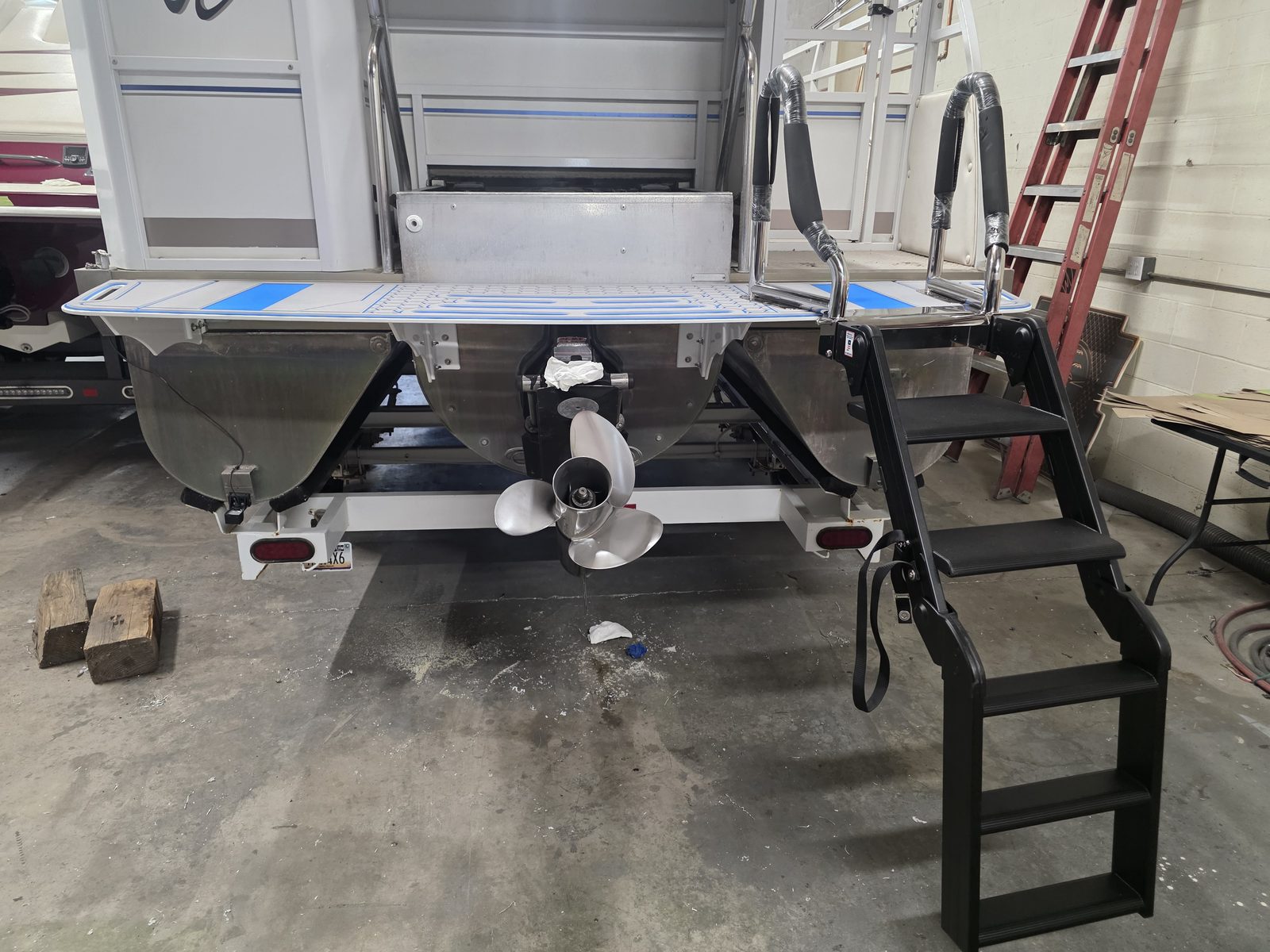 Wide angled boarding ladder with polished stainless handrails and black non-slip steps mounted beside the decking of a pontoon boat on a trailer