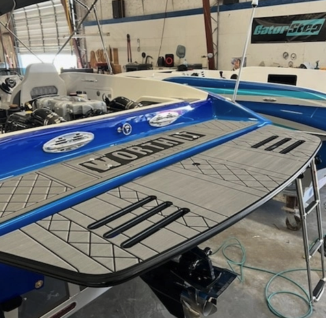 Custom gray non-slip swim platform with Moomba branding installed on a blue boat inside the Swim Platforms LHC fabrication shop