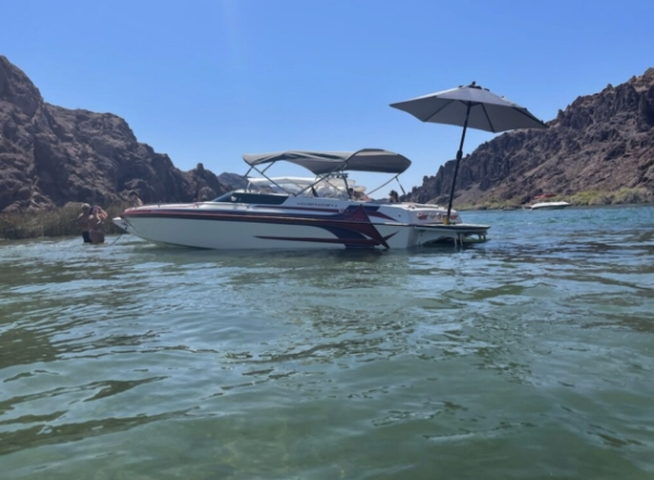 White and maroon performance boat anchored in a rocky cove with a Sandbar Shade umbrella extended over the swim platform