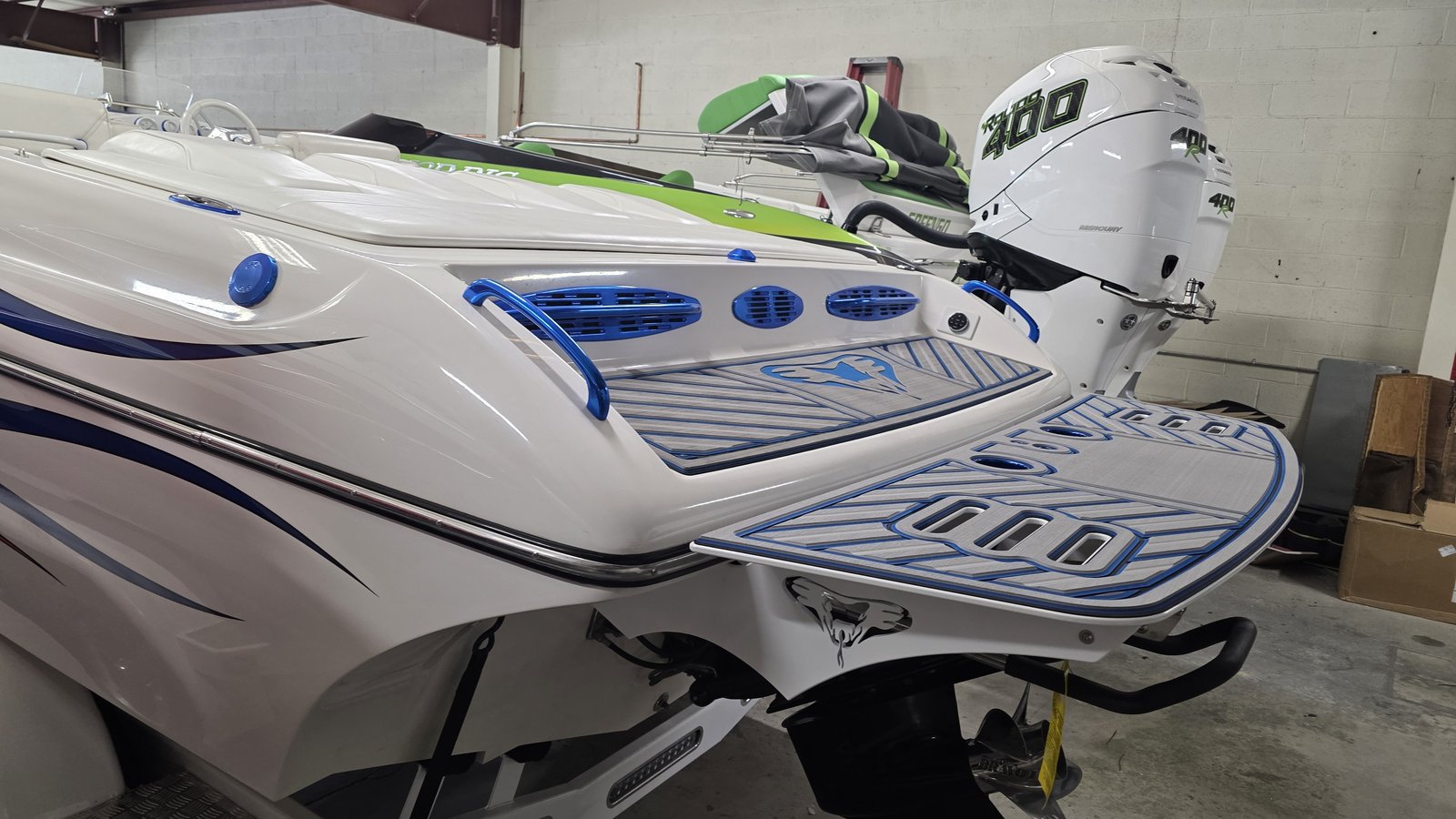 White and blue performance boat in the shop with an ultra-custom shaped swim platform finished in gray and blue decking featuring a bat logo