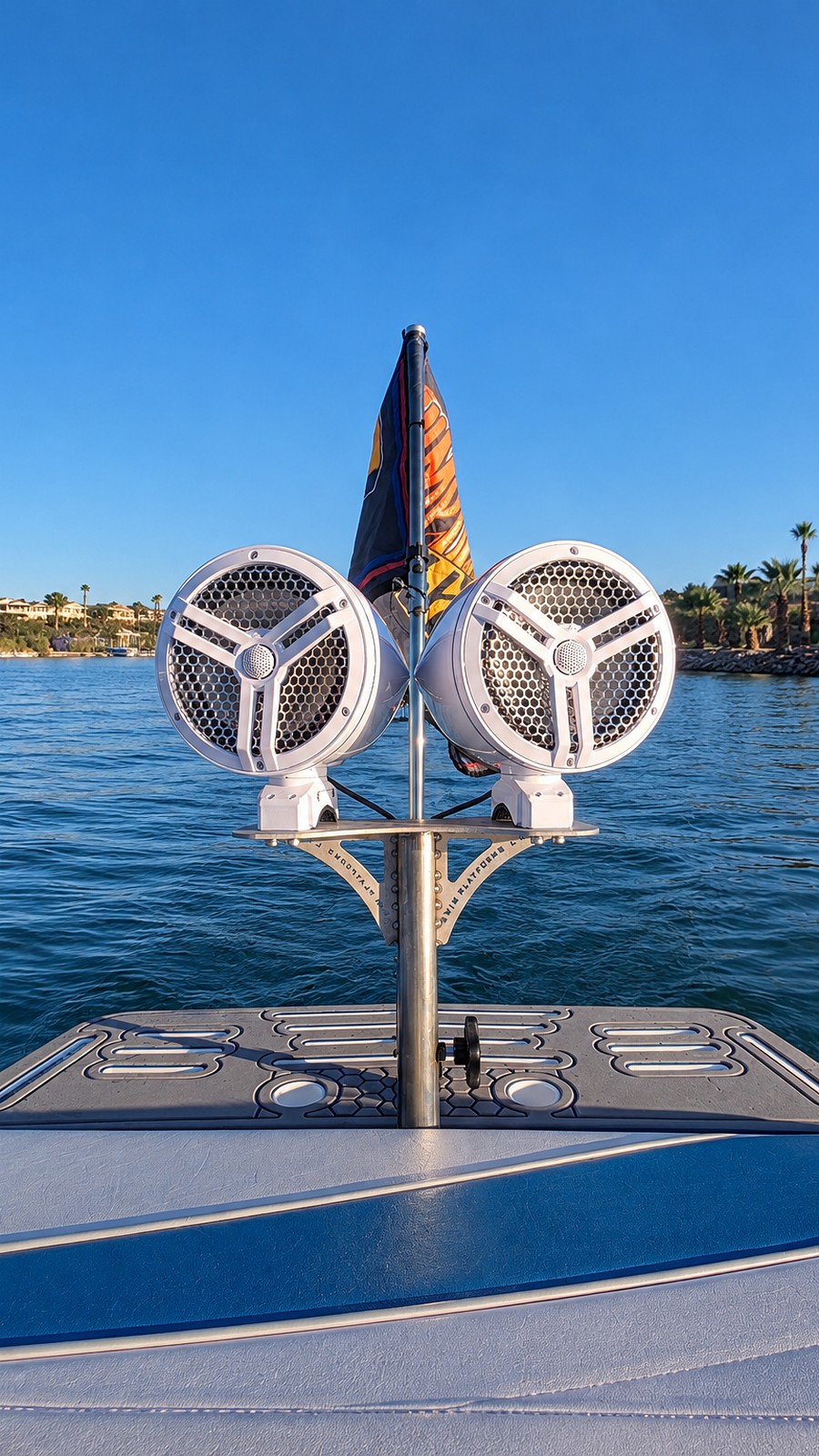 White marine speaker pods on a stainless steel mount and ski pole above a boat swim platform on the lake