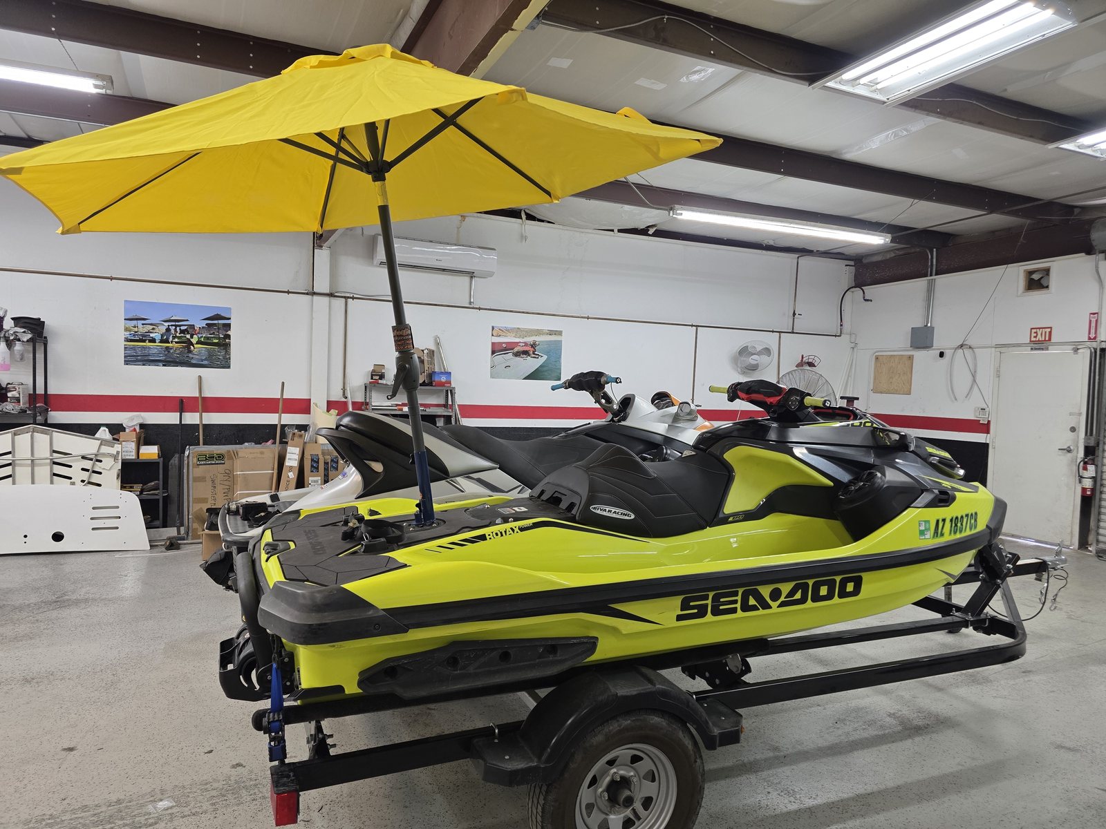 A neon green Sea-Doo on a trailer in the shop with a yellow Sandbar Shade umbrella mounted on its rear platform
