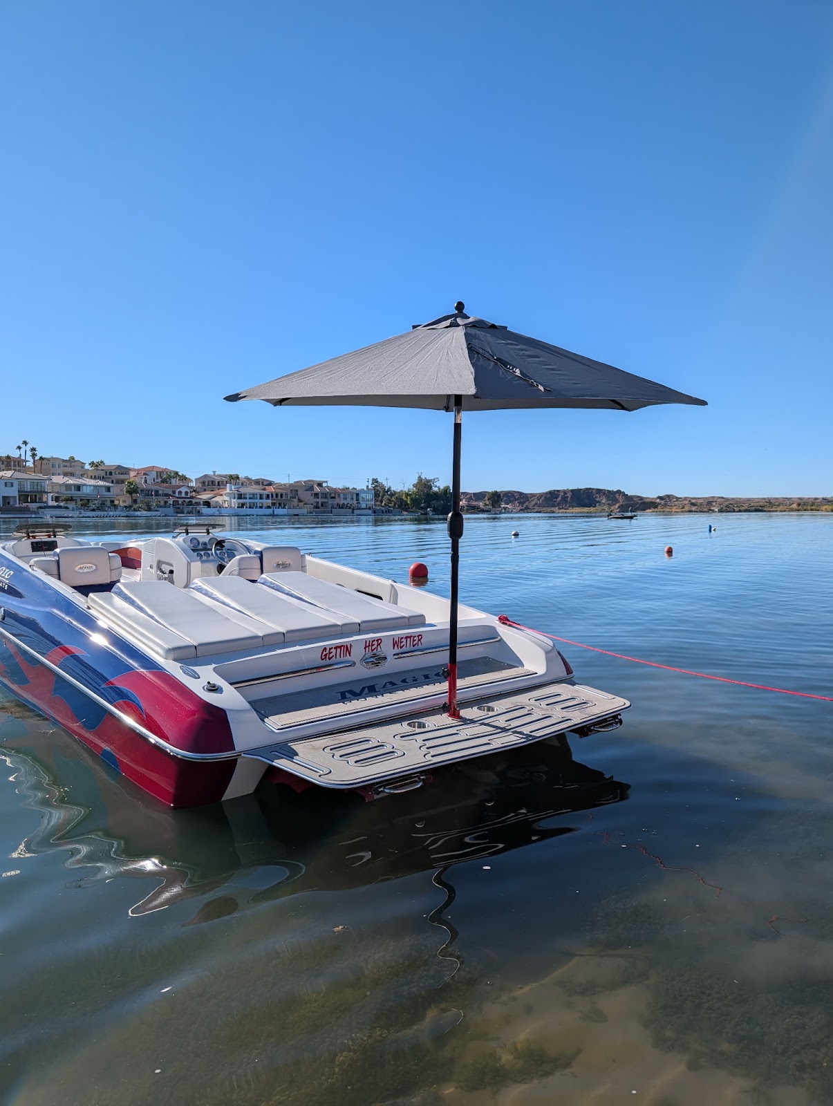 White and pink boat shaded by a gray Sandbar Shade umbrella on the lake